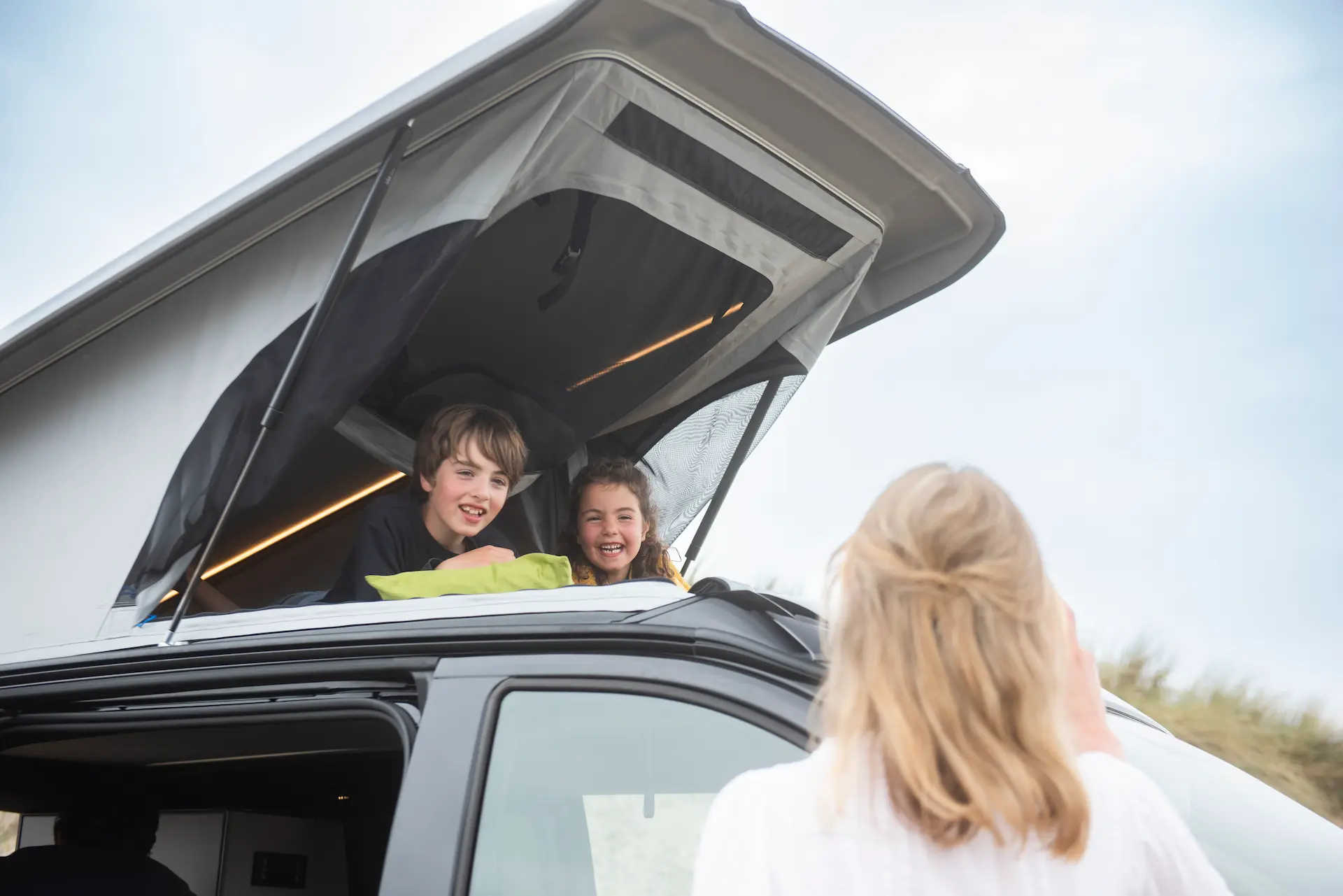 Buscamper met 4 slaapplaatsen en hefdak Hefdak met 2 kinderen bovenop de buscamper